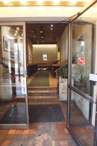 The inside of an entrance to a building with two glass doors. One of the doors is open. Beyond the doors are three steps that lead to a hallway.