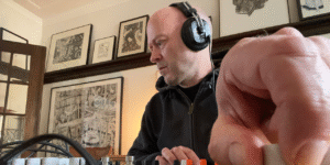 A photo of music artist Darren Stebeleski. He is wearing headphones and making music with a soundboard.