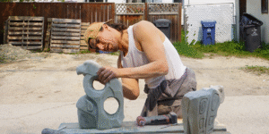 A photo of sculptor Fredrick Lyle Spence, working on a sculpture. He is standing in a backyard.
