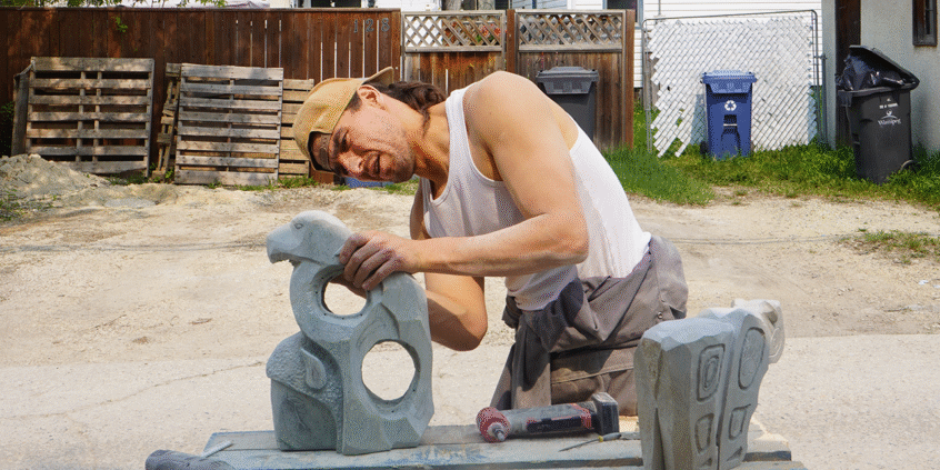 A photo of sculptor Fredrick Lyle Spence, working on a sculpture. He is standing in a backyard.